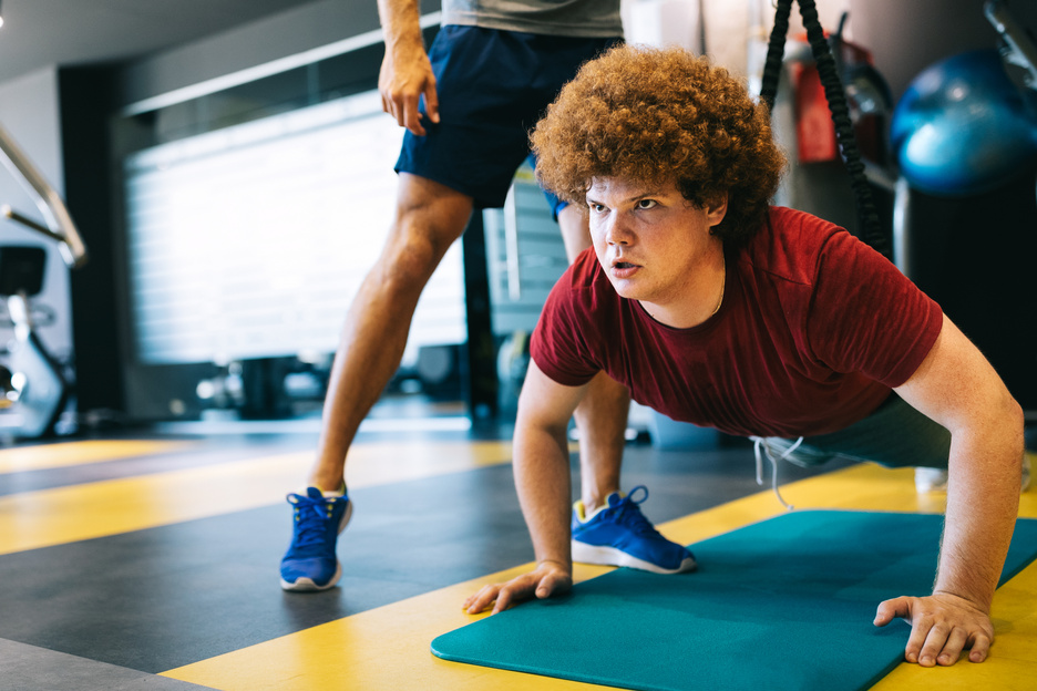 Fat young men with trainer exercising at fitness gym.